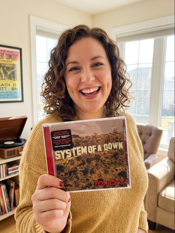 Person holding a 'System of a Down' album in a living room.