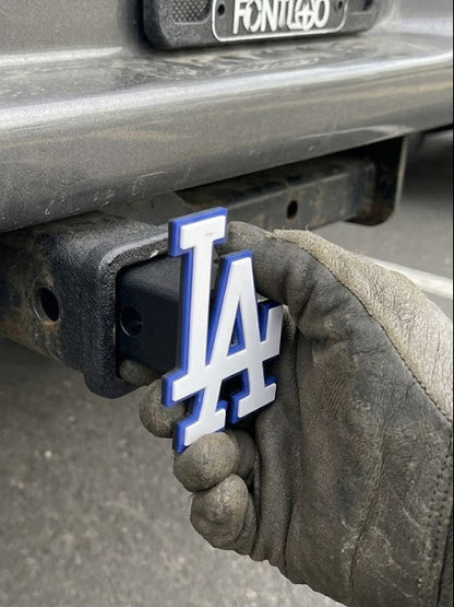 Hand holding a Los Angeles Dodgers logo on a vehicle's hitch receiver.