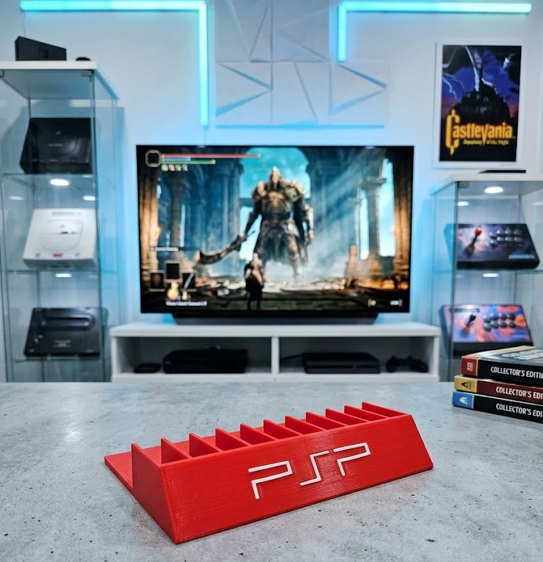 Red PSP console stand in front of a television displaying a video game in a gaming room.