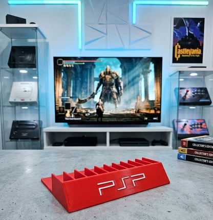 Red PSP console stand in front of a television displaying a video game in a gaming room.